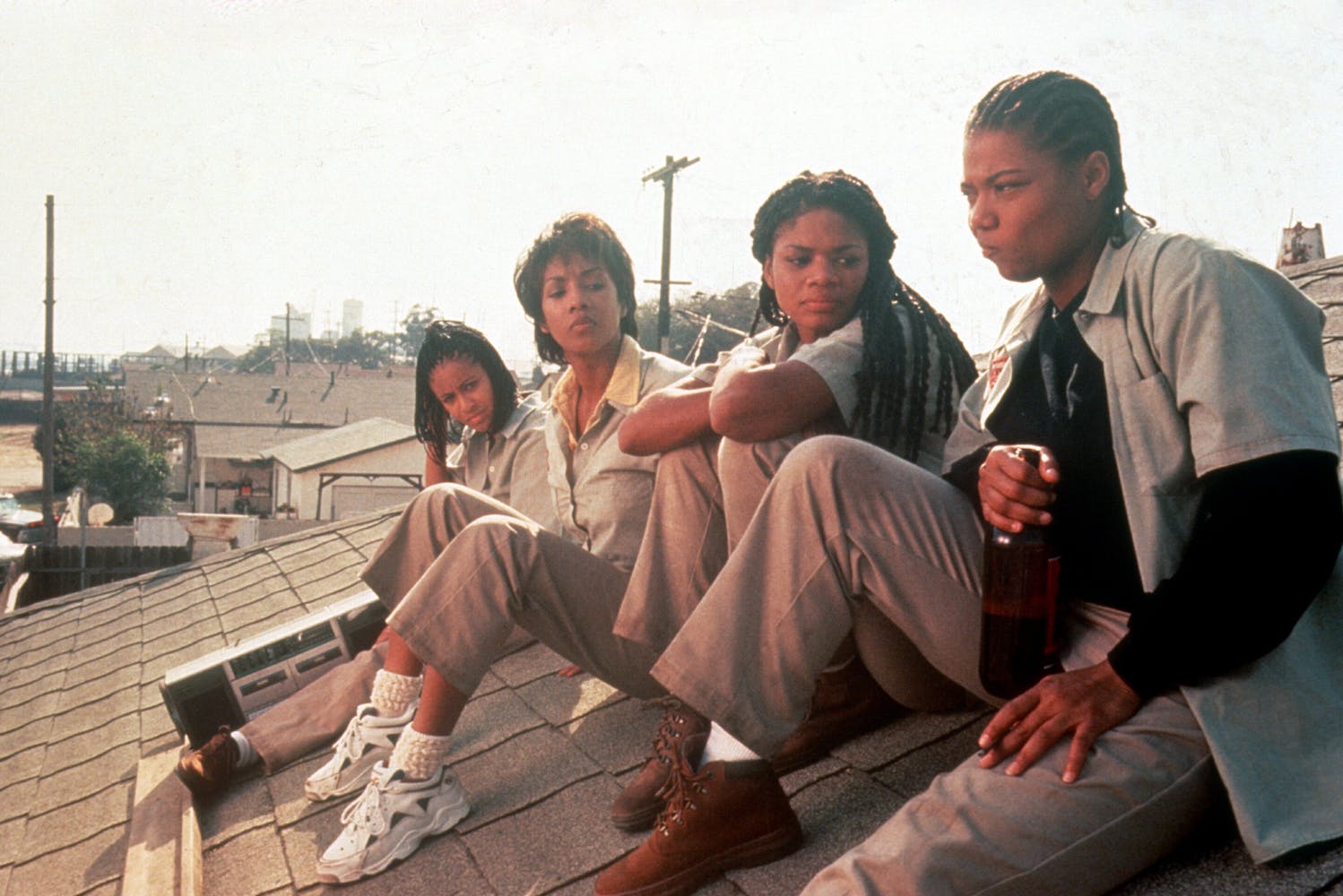 Four women in beige uniforms sit on a roof together, drinking beer and listening to music.
