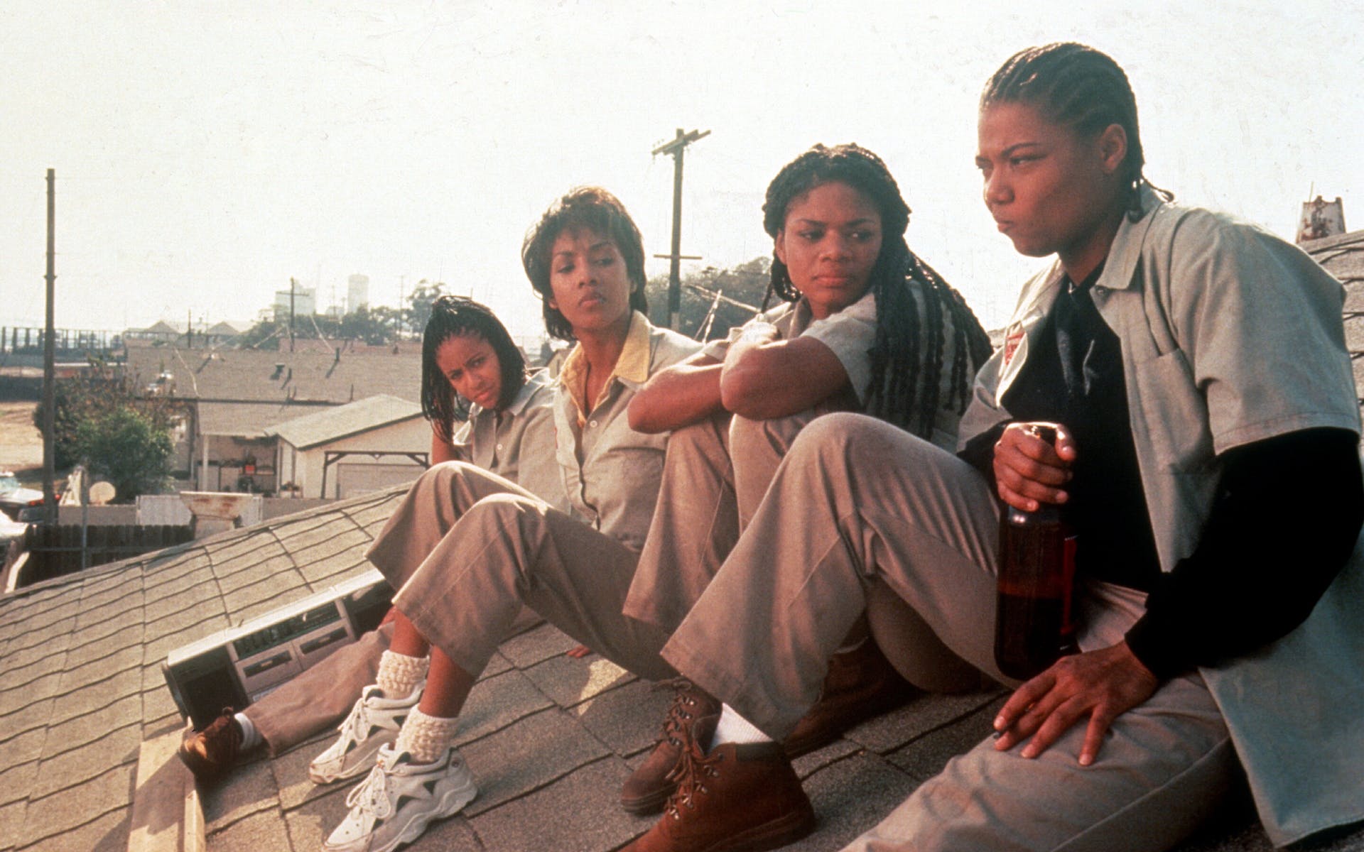 Four women in beige uniforms sit on a roof together, drinking beer and listening to music.
