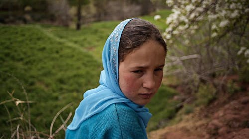 A girl in a blue headscarf sits in a field.