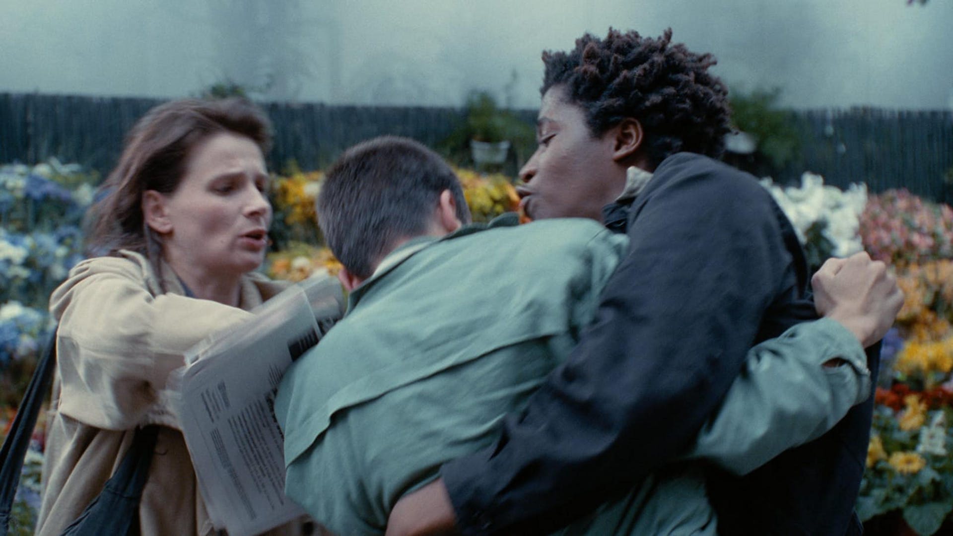 Three people blurred and tangled together in movement on the street in front of a floral stand.