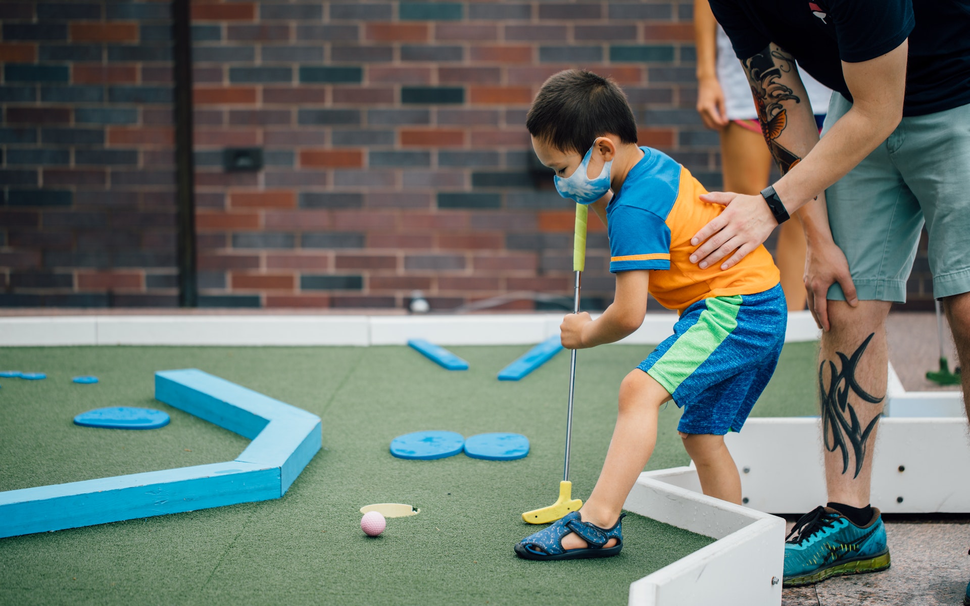 A young boy plays Skyline Mini Golf with the help of an adult.