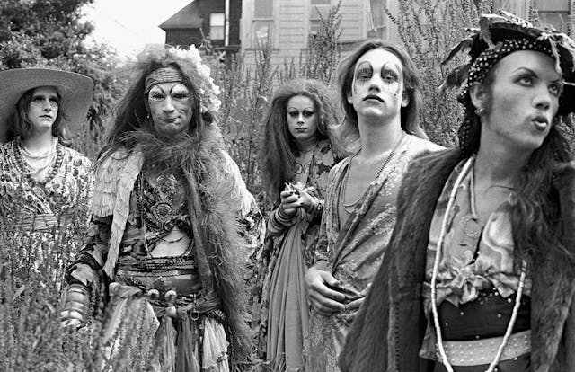 Five drag performers in a field in front of a house