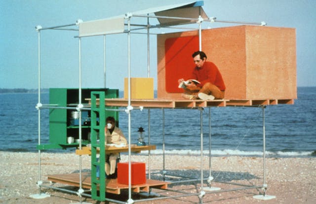 Two men sitting in a two-story structure made of metal poles and wooden panels on the beach