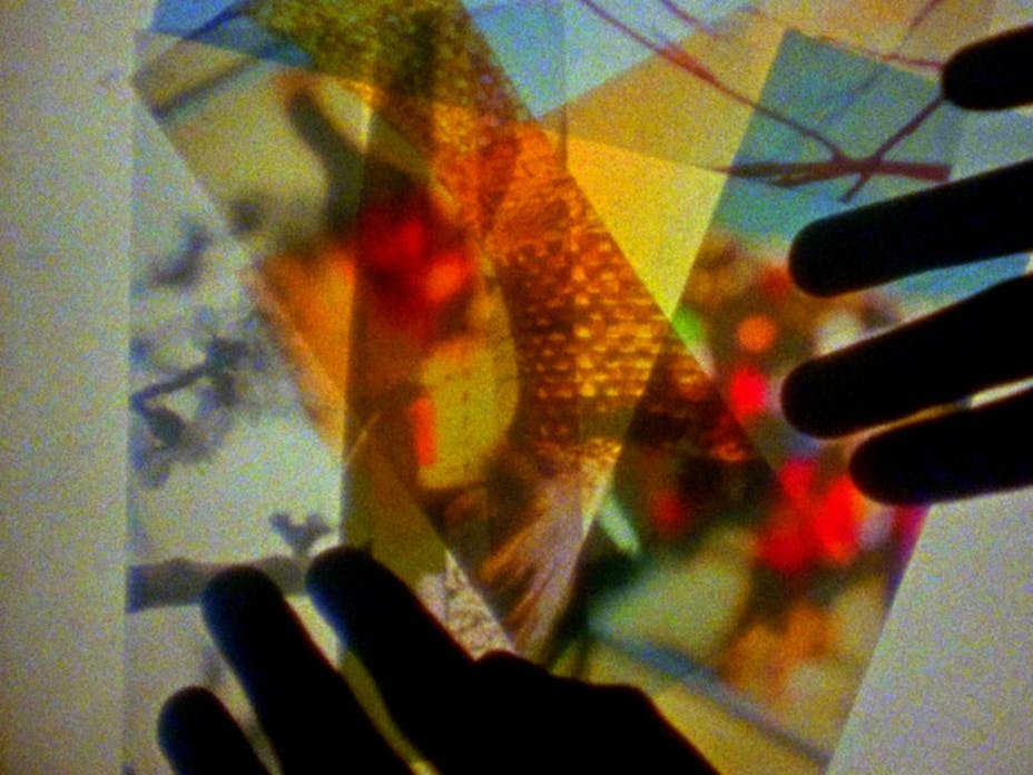 Still of hands moving cutout rectangular bright colored image transparencies over a lightbox.