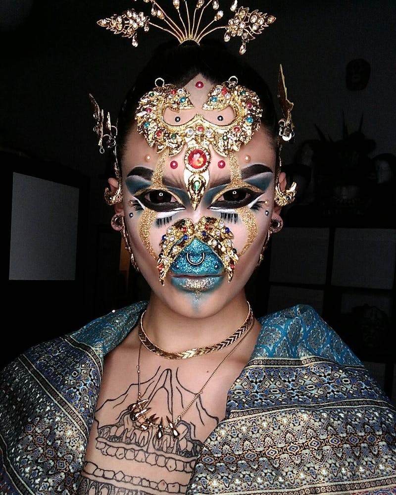 A person wearing geometric alien-like make-up looks at the viewer.