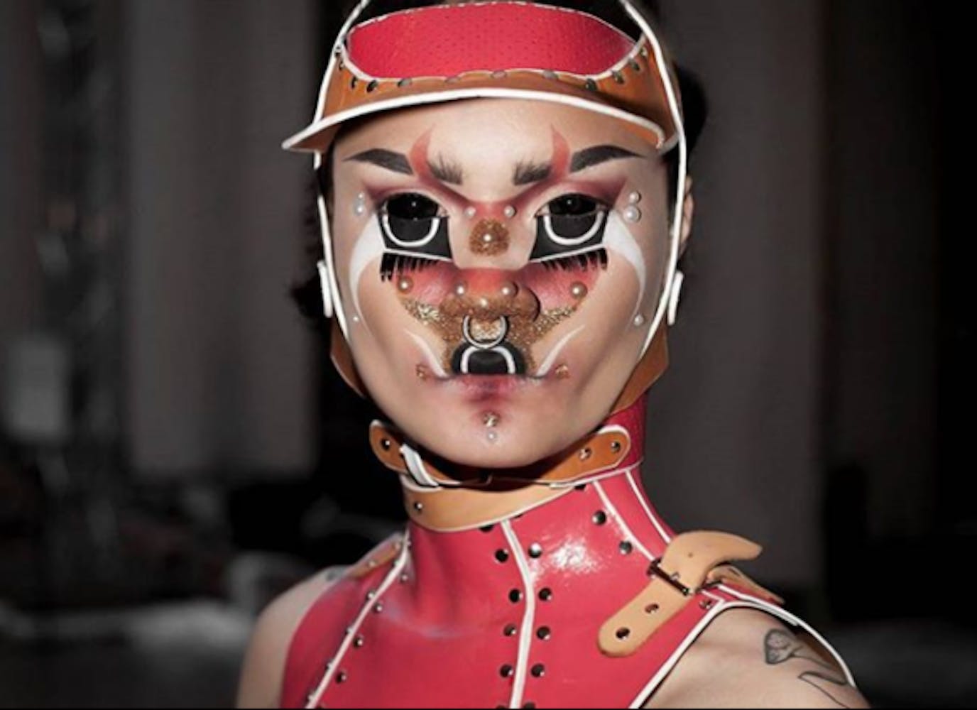 A person wearing geometric alien-like make-up looks at the viewer.