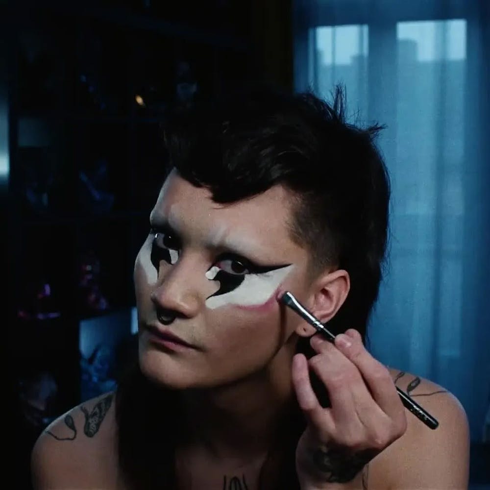 A person applies make-up to their face while looking at the viewer.