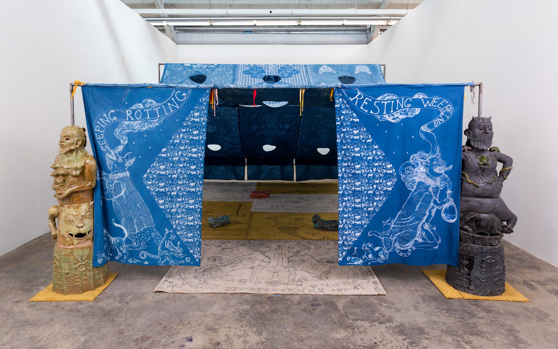 Image of tent made of blue patterned cloth in gallery with statues on either side