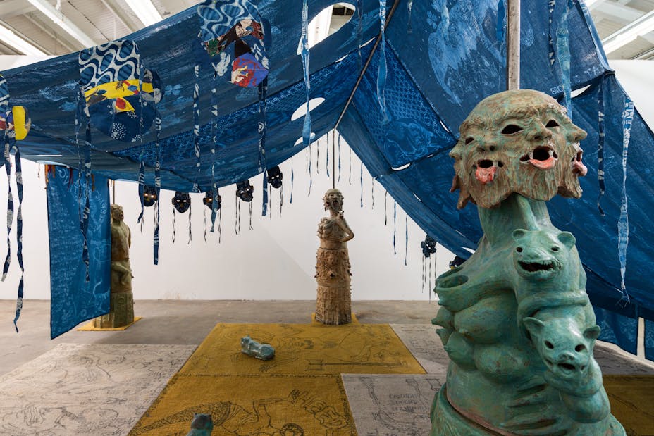 Image of tent made of blue patterned cloth in gallery with statues on either side
