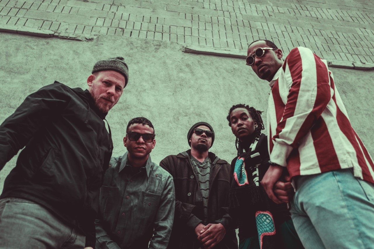 Five musicians standing in front of a wall