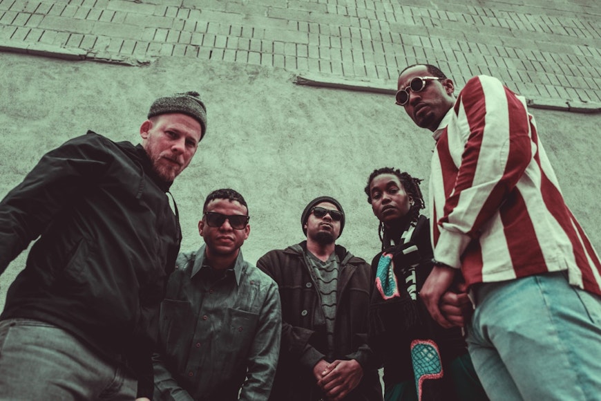 Five musicians standing in front of a wall