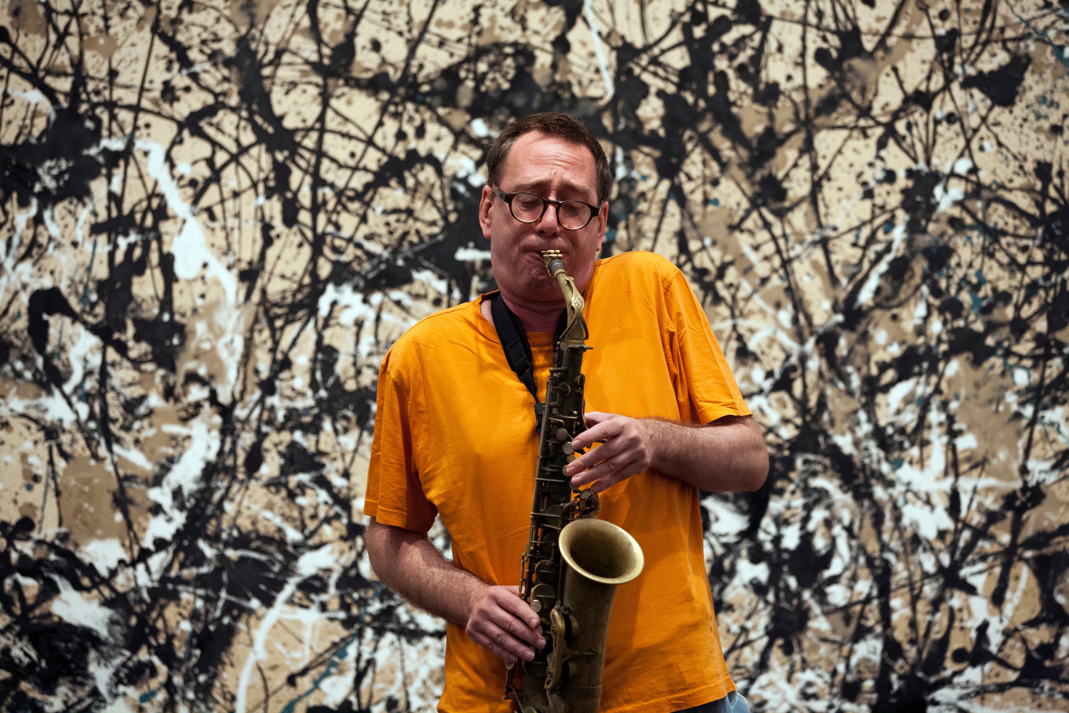 John Zorn plays an alto saxophone in front of a Jackson Pollock painting.