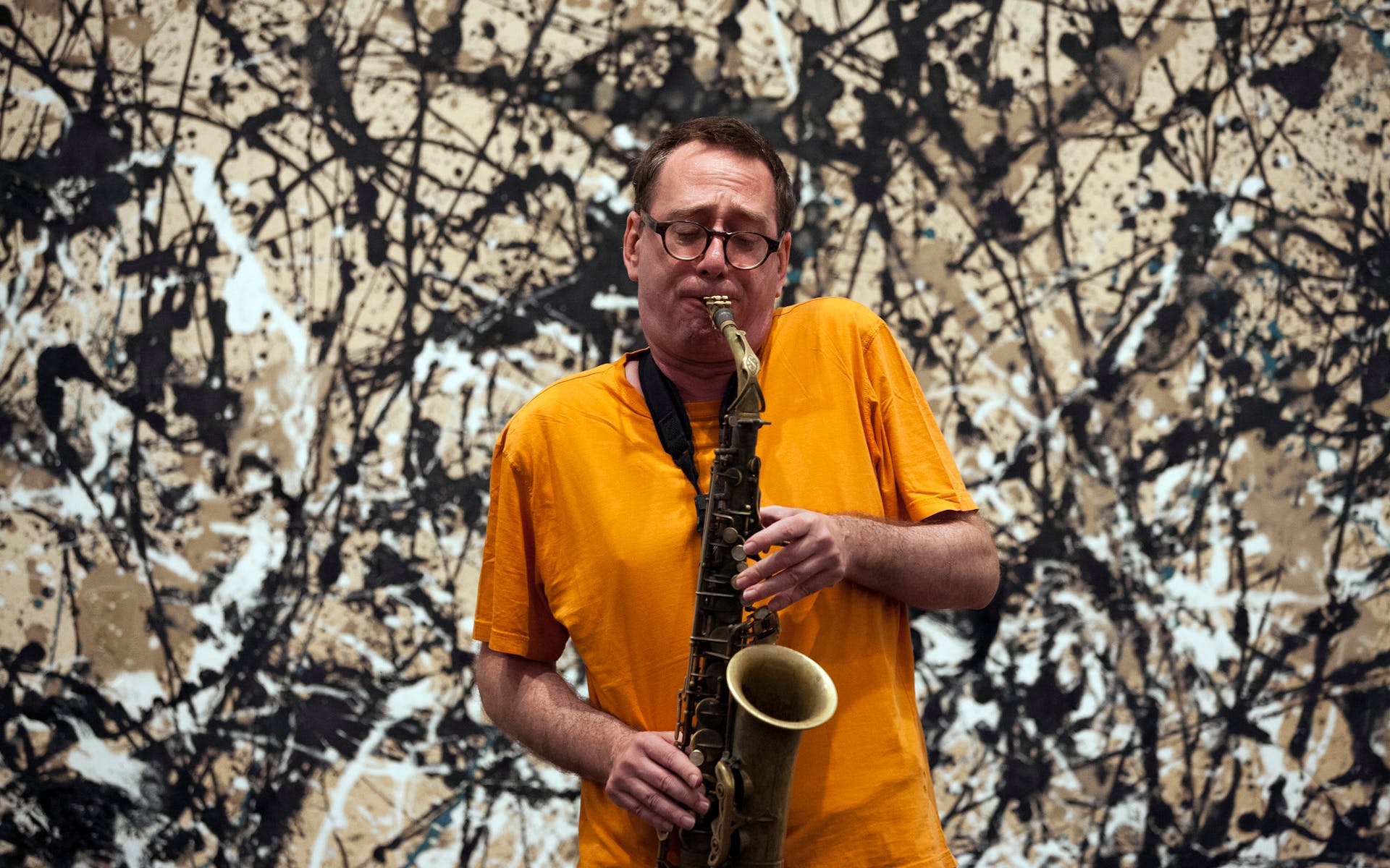 John Zorn plays an alto saxophone in front of a Jackson Pollock painting.