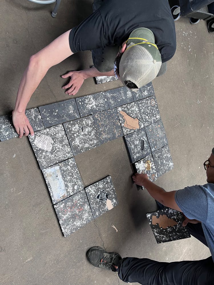 Two adults lay out ceramic tile like artworks on the ground.