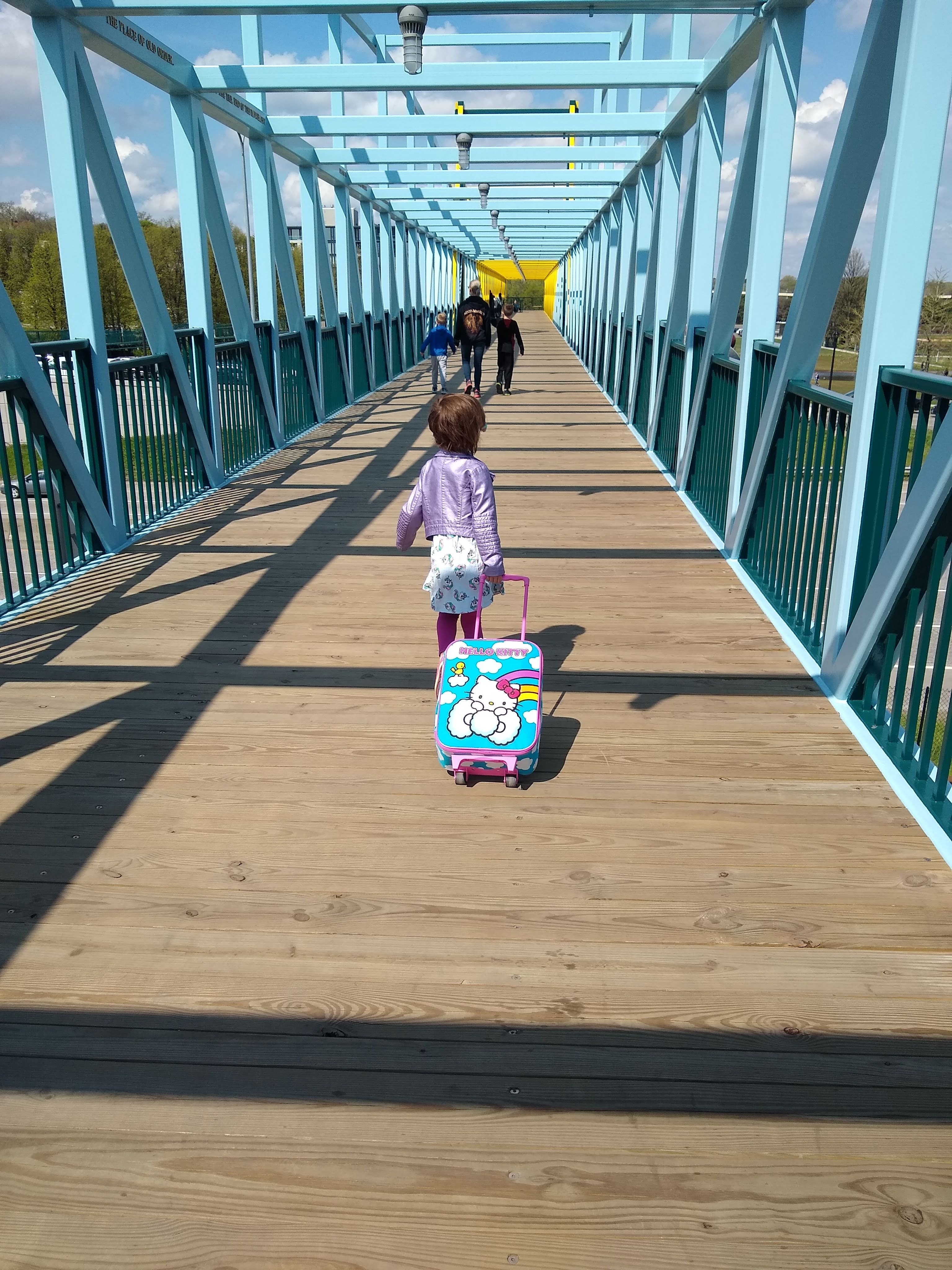 A young girl pulls a rolling luggage bag across a walking bridge