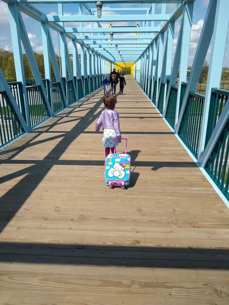 A young girl pulls a rolling luggage bag across a walking bridge