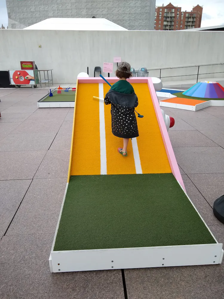 A girl holding a mini golf club stands on a mini golf course.
