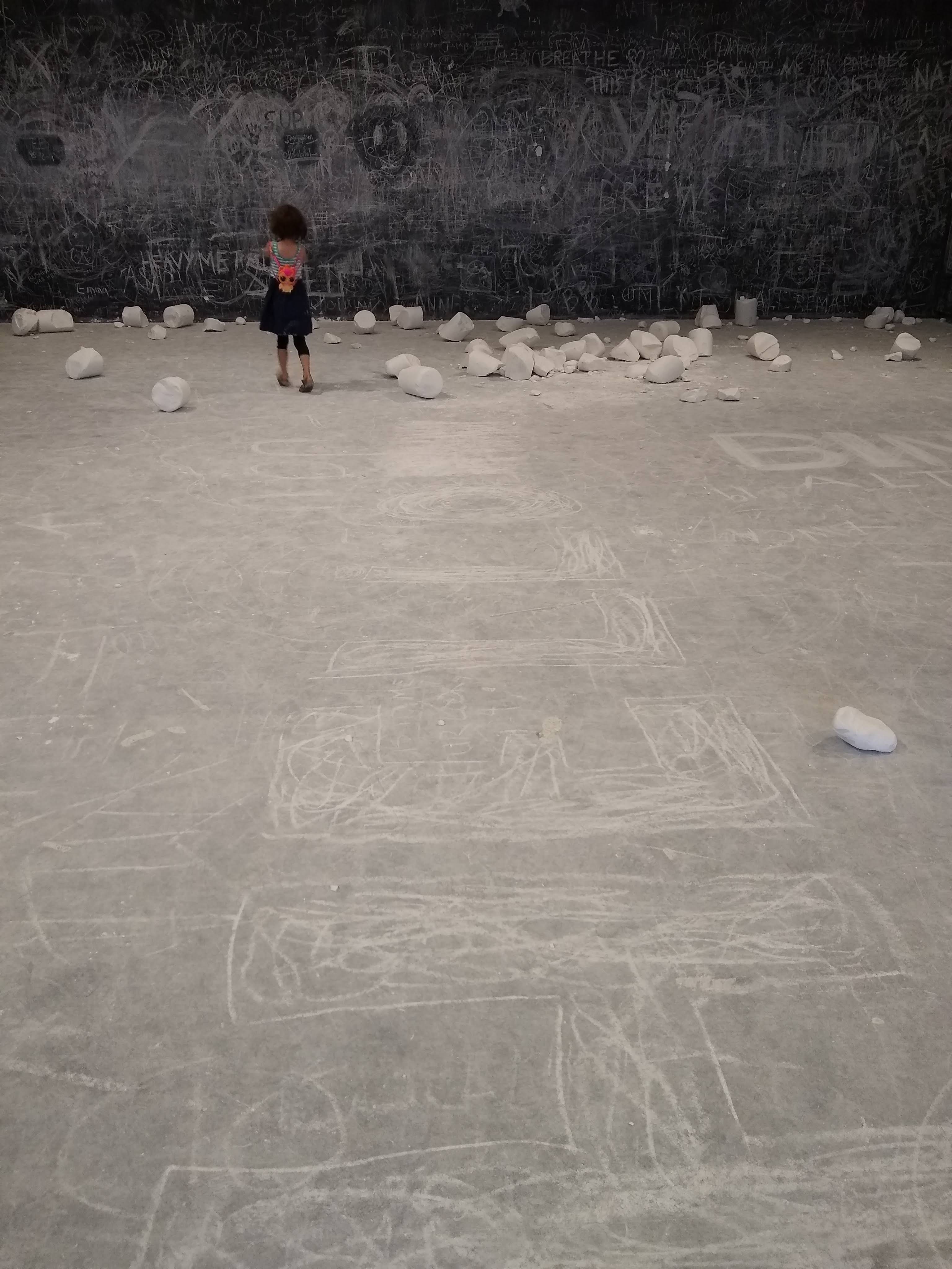 A girl stands in a gallery surrounded by large chunks of chalk.