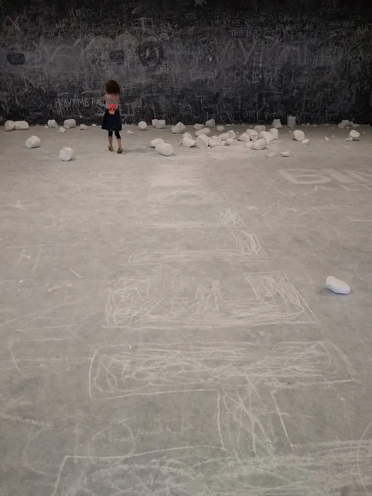 A girl stands in a gallery surrounded by large chunks of chalk.