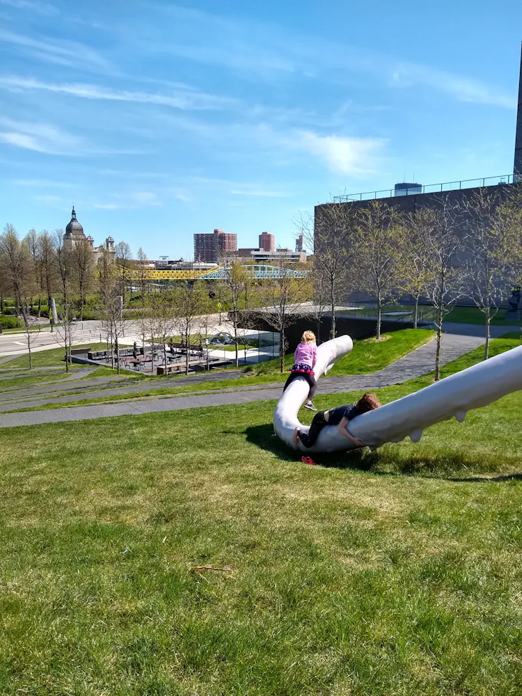 A girl cilmbs on a metal tubluar sculpture outside in a park.