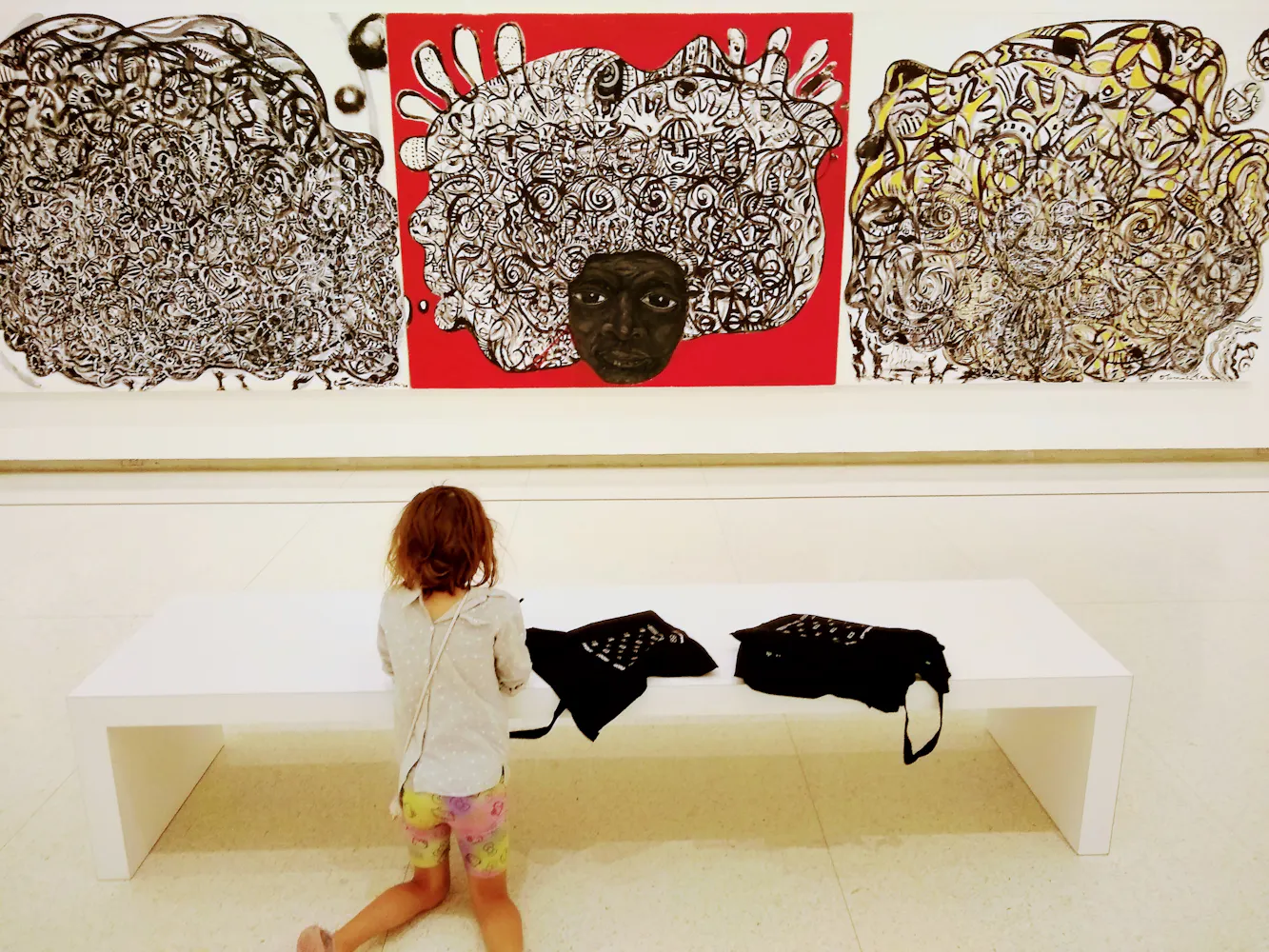 A girl makes a drawing in front of a large tripich painting in a gallery.