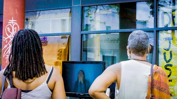 Two adults watch a monitor set up outside.