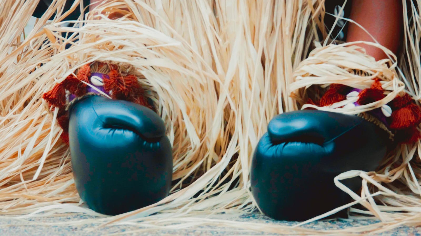 Hands in boxing gloves touch the ground with staw draped behind them.