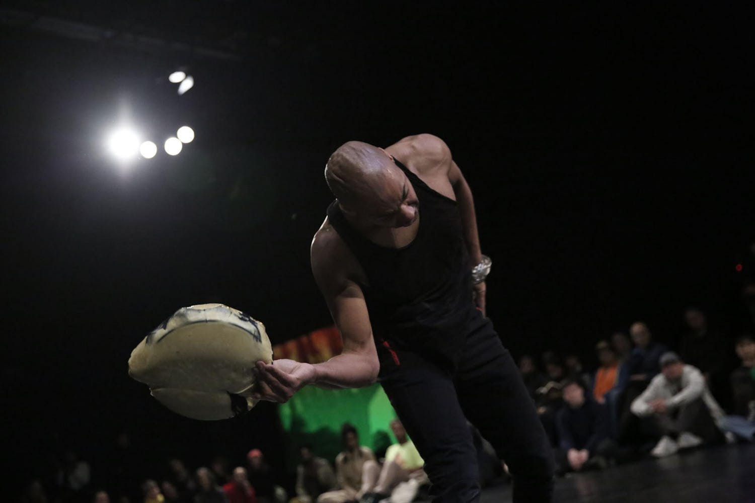 A person with dark skin holding a drum dances with their back to the audience.