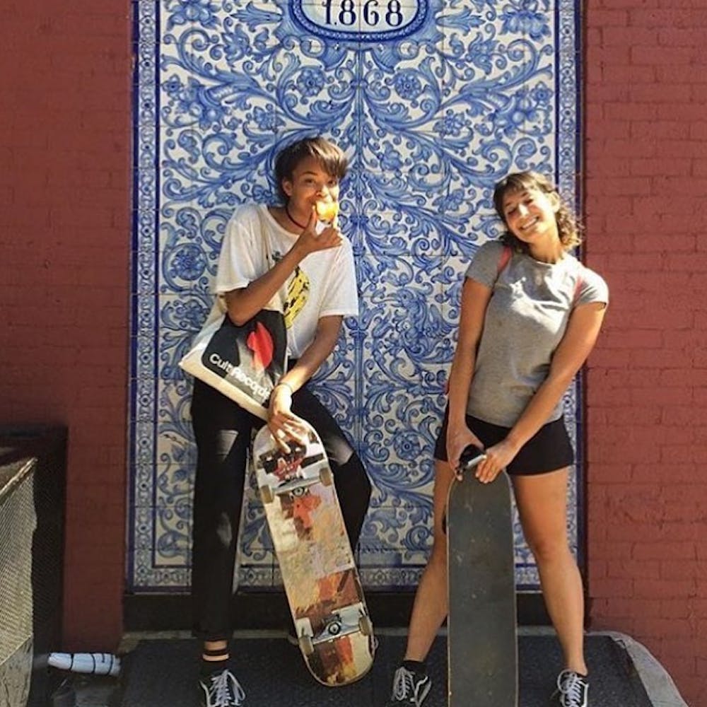Two young adults hold skateboards and smile at the viewer.