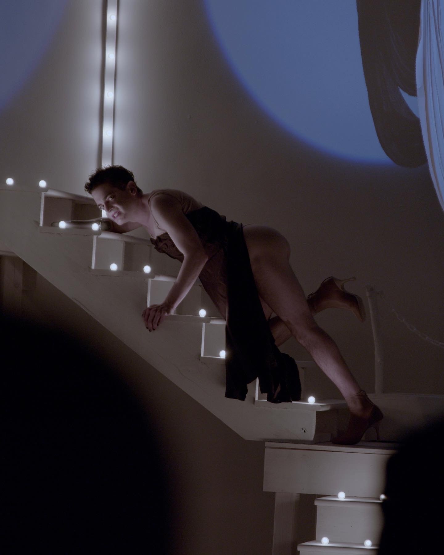 An adult in a black dress crawls up a white staircase that has been outfitted with white lights.
