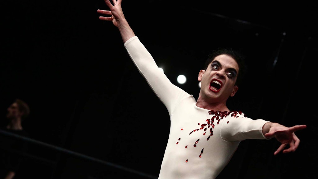 An adult with lipstick and smeared eye make-up points and screams with wearing a ballet top adored with red jewels.