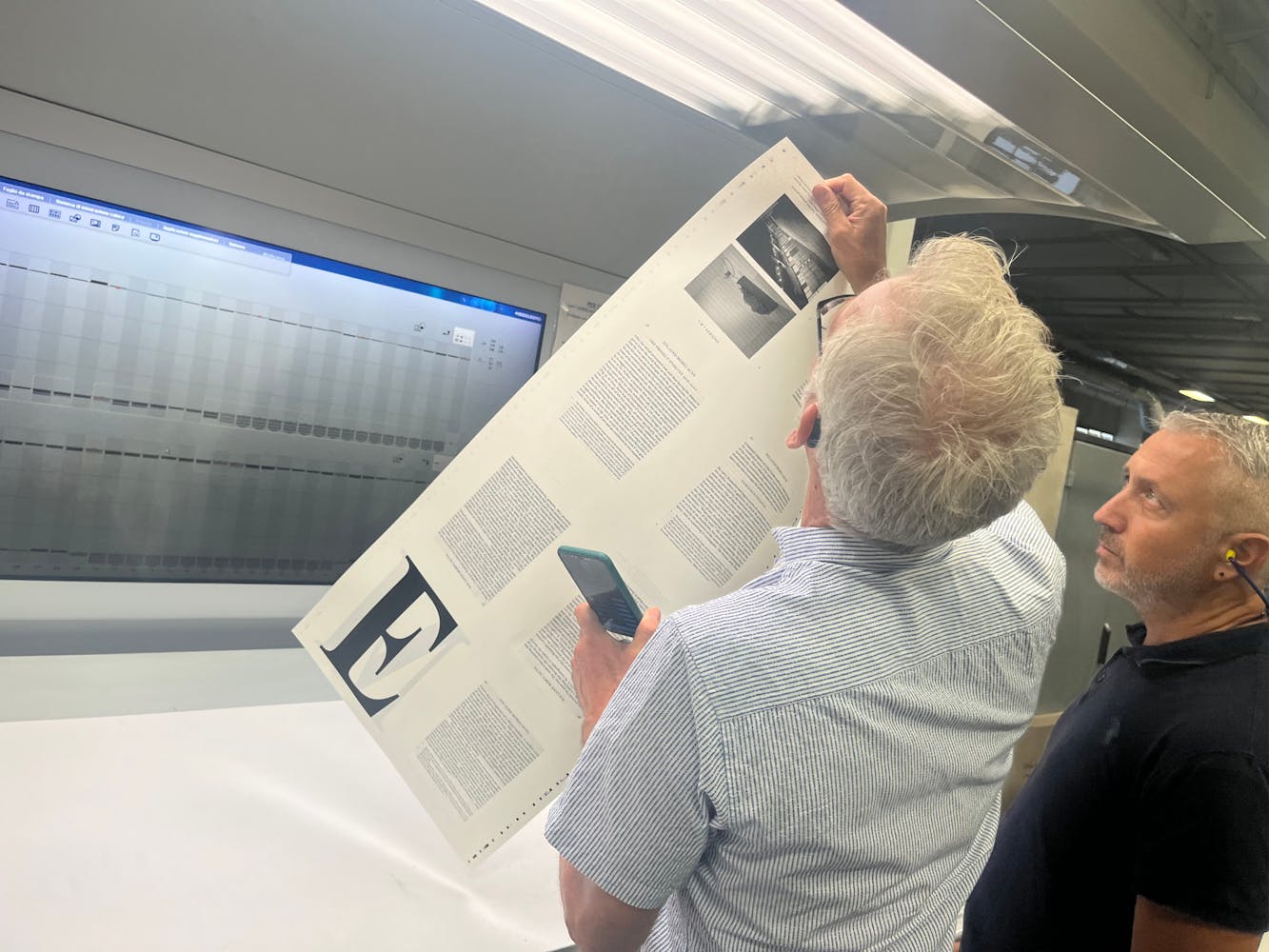 A man holds up a print sheet and examines it.