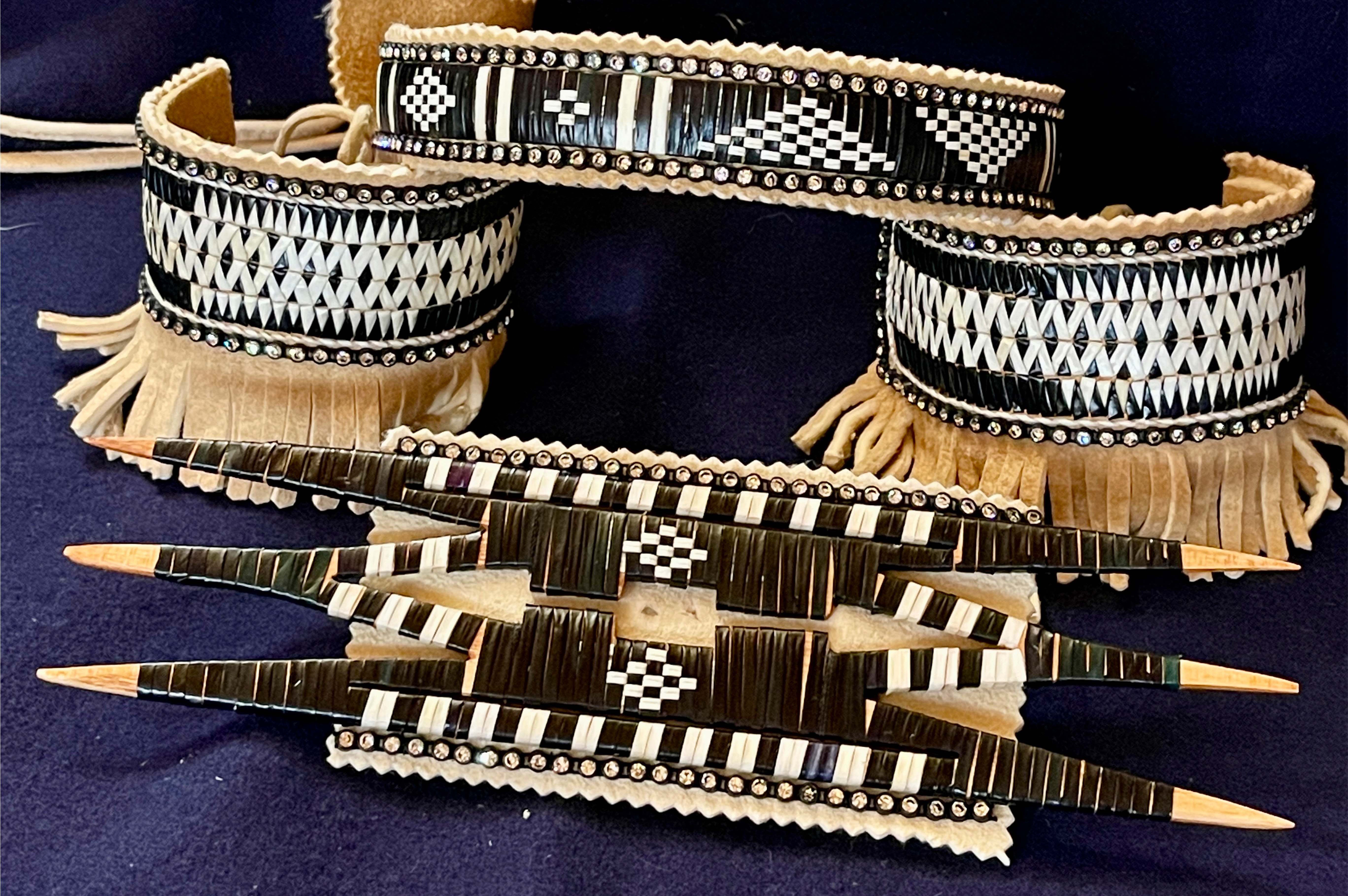 Woven quillwork designs on wood and leather pieces with detailed graphic patterns in black and white, photographed together on a dark blue blanket.