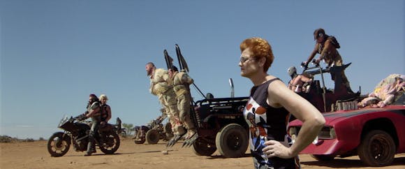 still from Mad Max of a battalion in the desert with an image of a person superimposed into the frame, hands on hips.