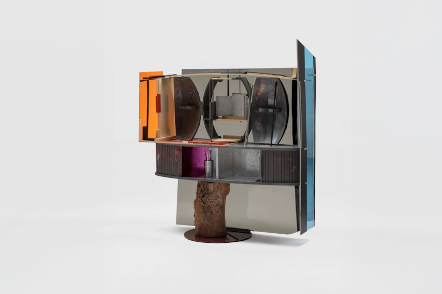A multi-piece silver cabinet with colorful pops of orange, pink and blue on the sides and back. It balances on a wooden stump.