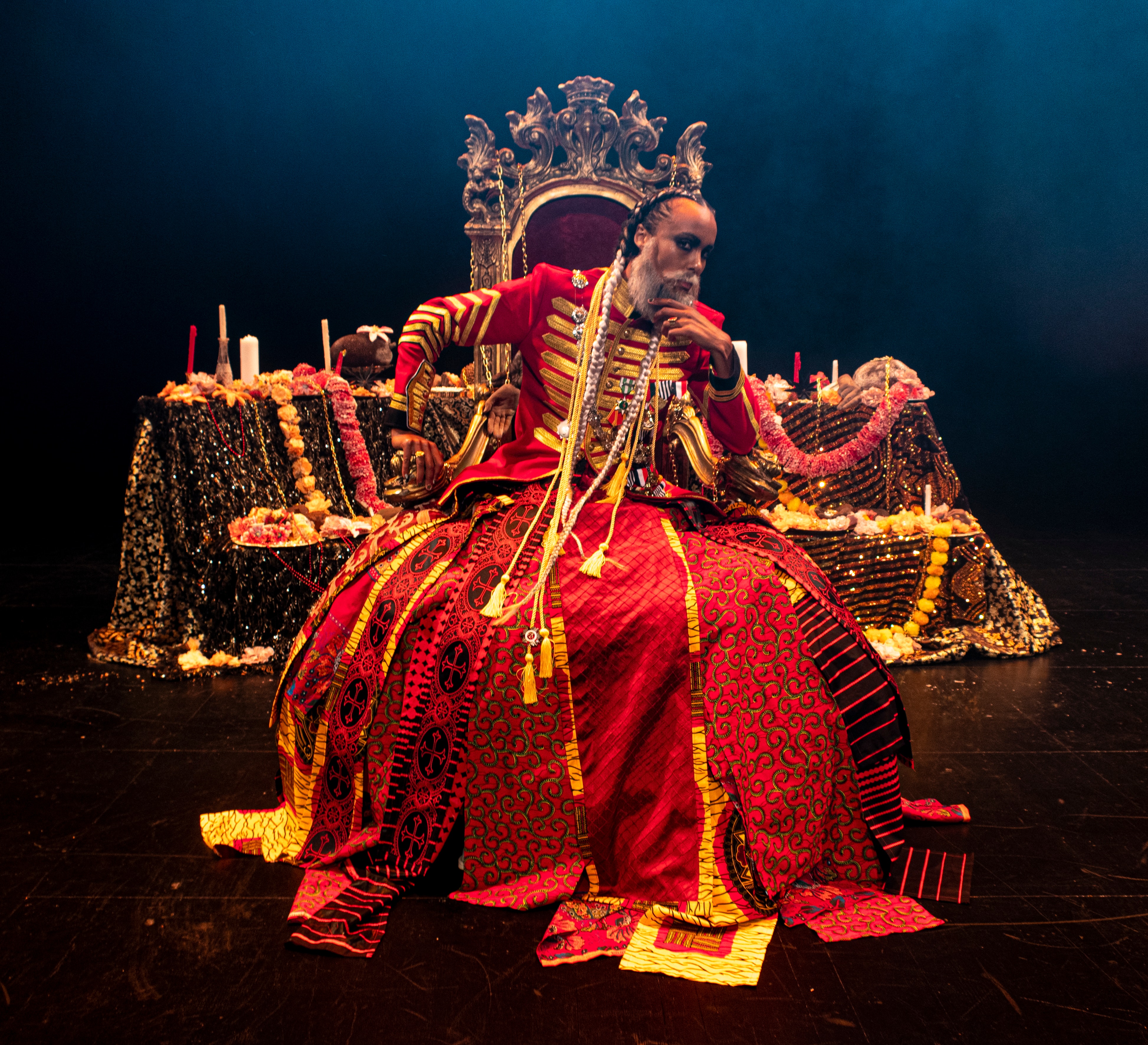 Person wearing large red uniform/dress sitting on throne on dark stage