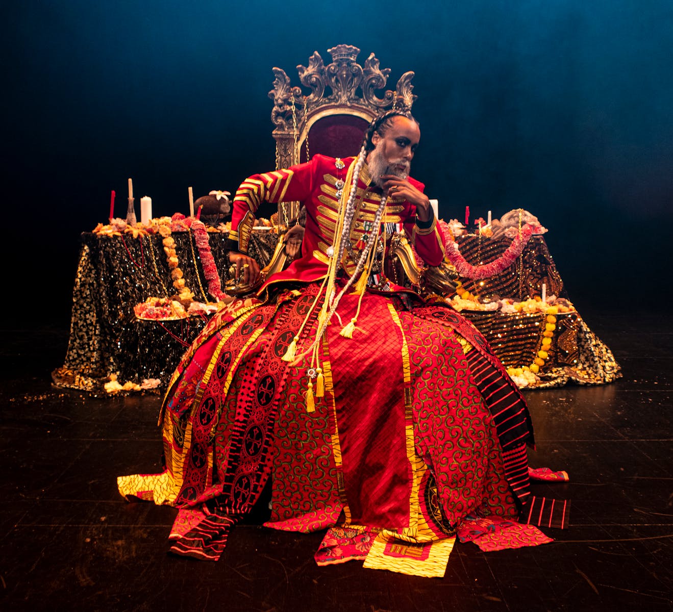Person wearing large red uniform/dress sitting on throne on dark stage