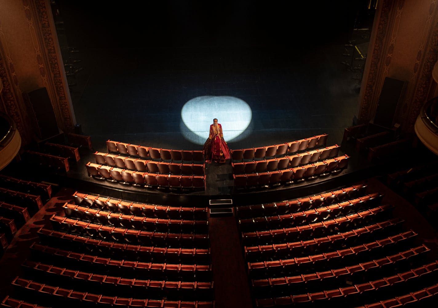 Theater stage and seating with one person at the front of the stage with a spotlight behind them