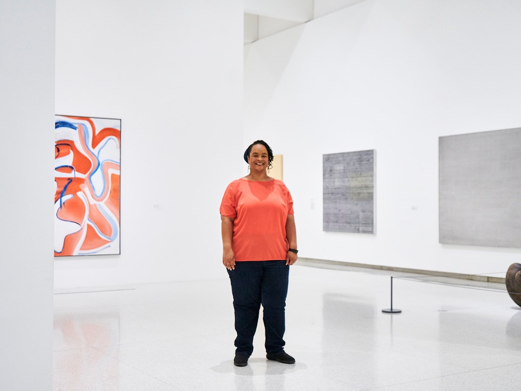 A woman stands in a gallery of paintings smiling at the viewer.