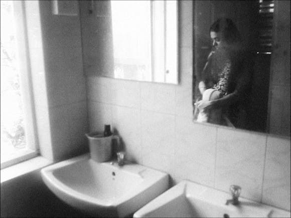 image of a bathroom wash area with the reflection of a woman in the mirror.