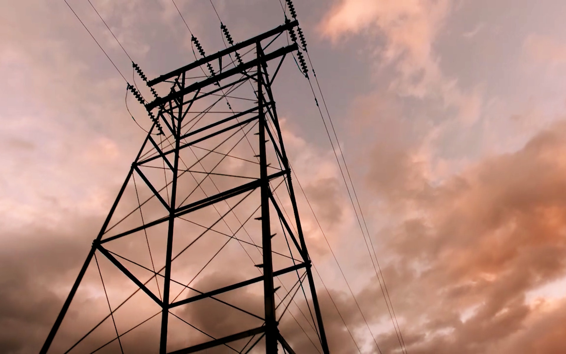A high power line tower stands in front of a clowdy sky.