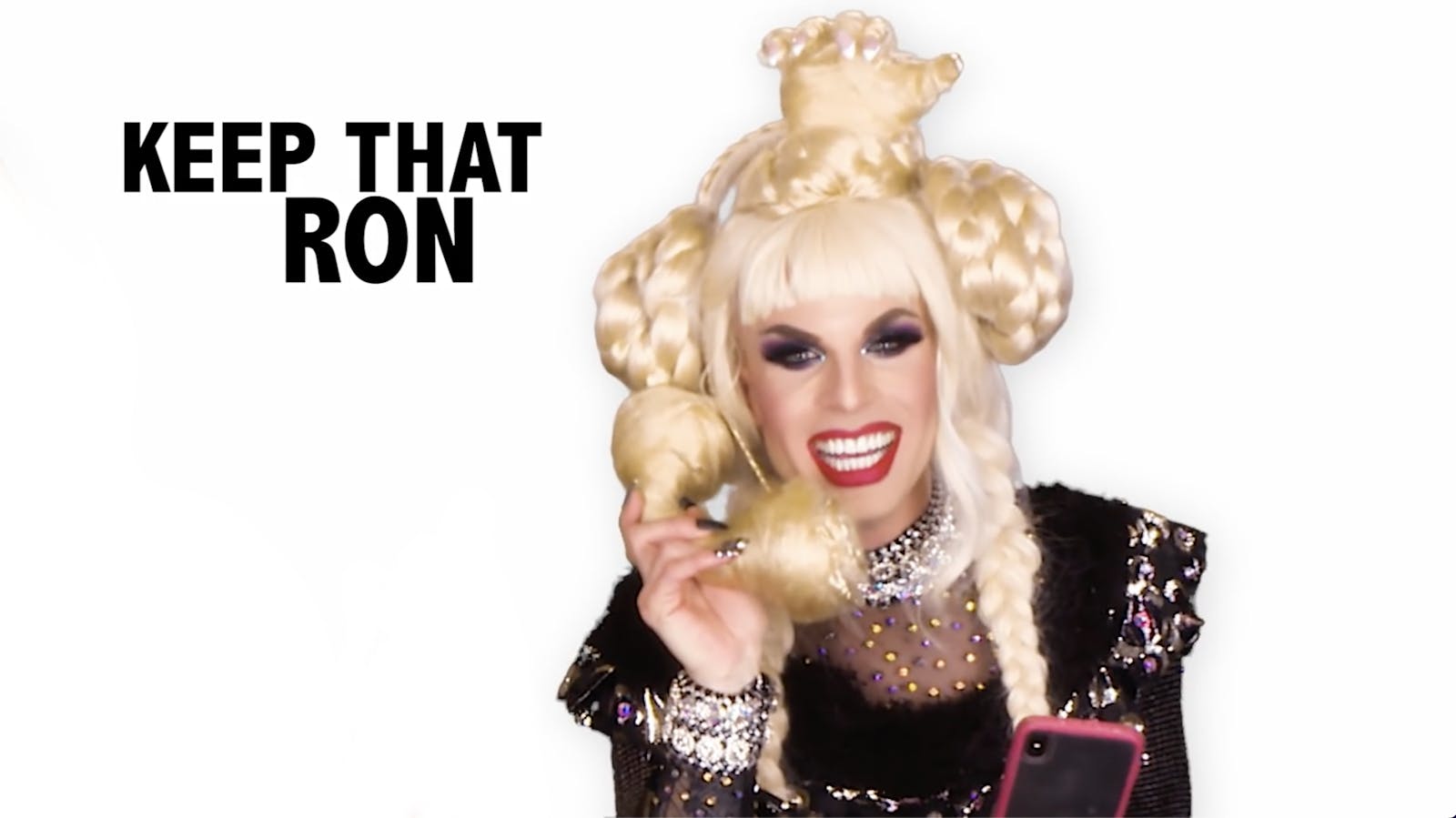 A drag queen talks into a phone made out of hair that is connected to her wig in a white room with the words 