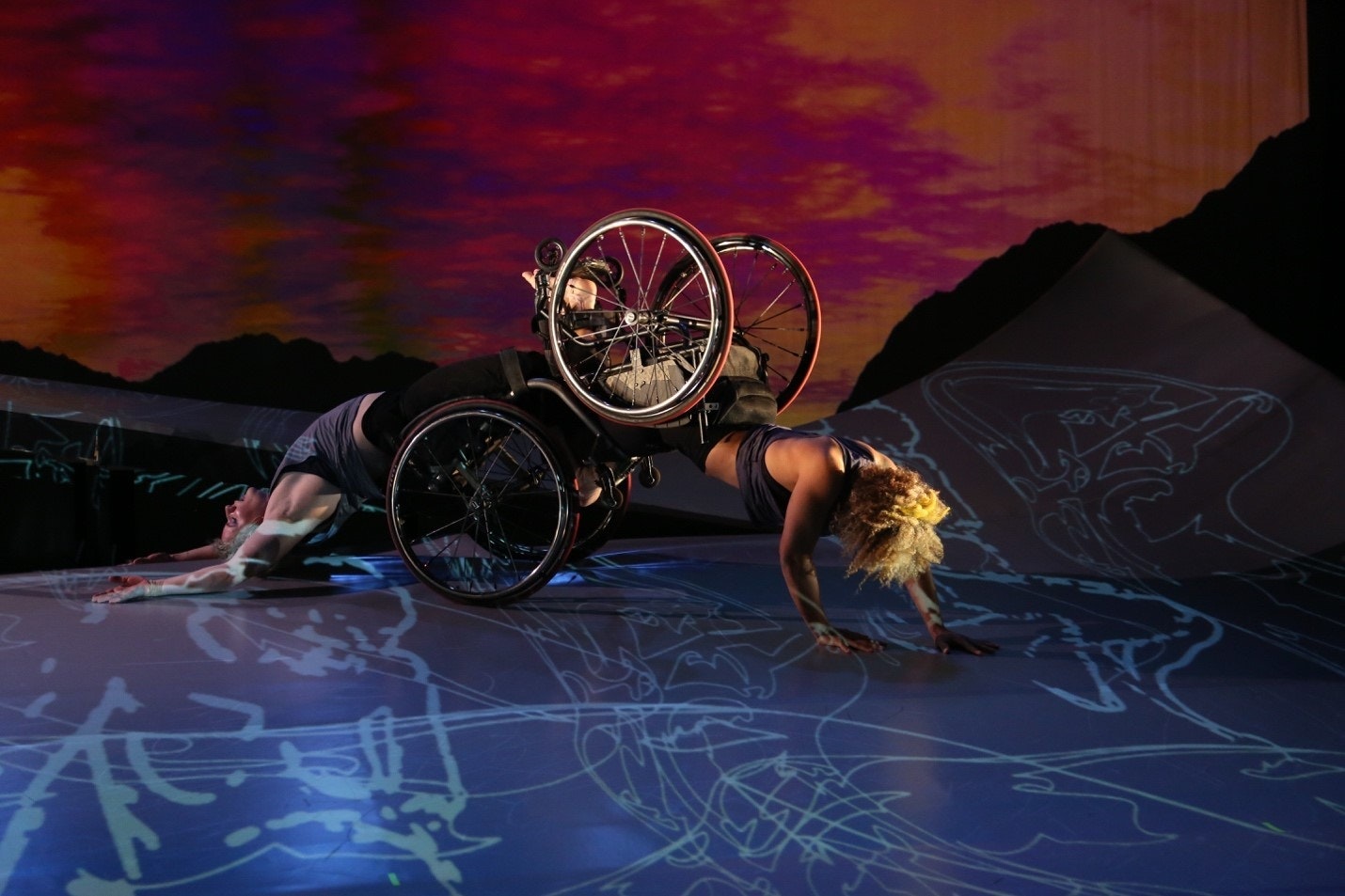 Alice Sheppard, a light-skinned Black woman with a crown of short curly hair, is crawling on her hands with her knees in Laurel Lawson's footplate. Laurel, a white woman, is arching her back on the ground as she is dragged along the floor. A sunset appears behind them.