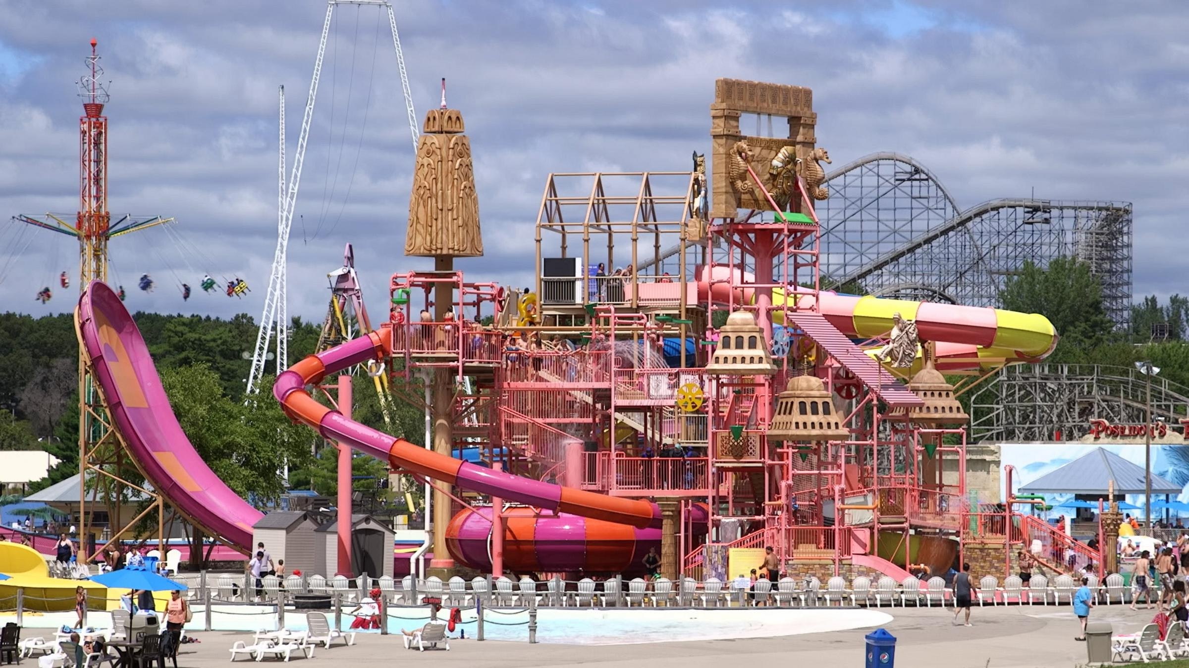 A photo of an entire outdoor waterpark, in bright colored in pink, yellow and orange. There are roller coasters and swing rides in the background.