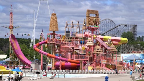A photo of an entire outdoor waterpark, in bright colored in pink, yellow and orange. There are roller coasters and swing rides in the background.
