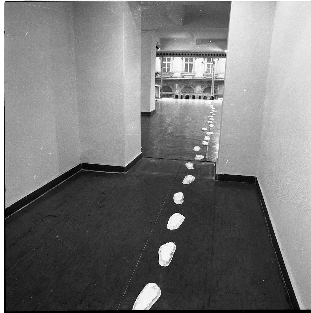 Black and white photograpgh of white footprints leading out an empty gallery.