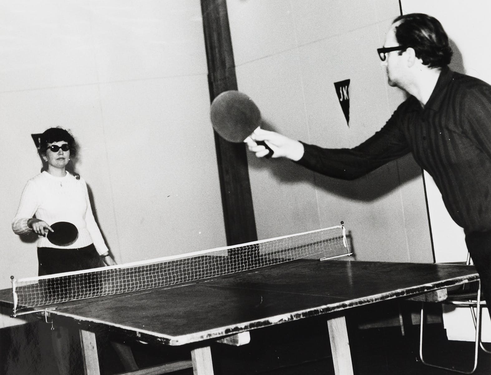 Two adults play ping pong in a black and white photograph