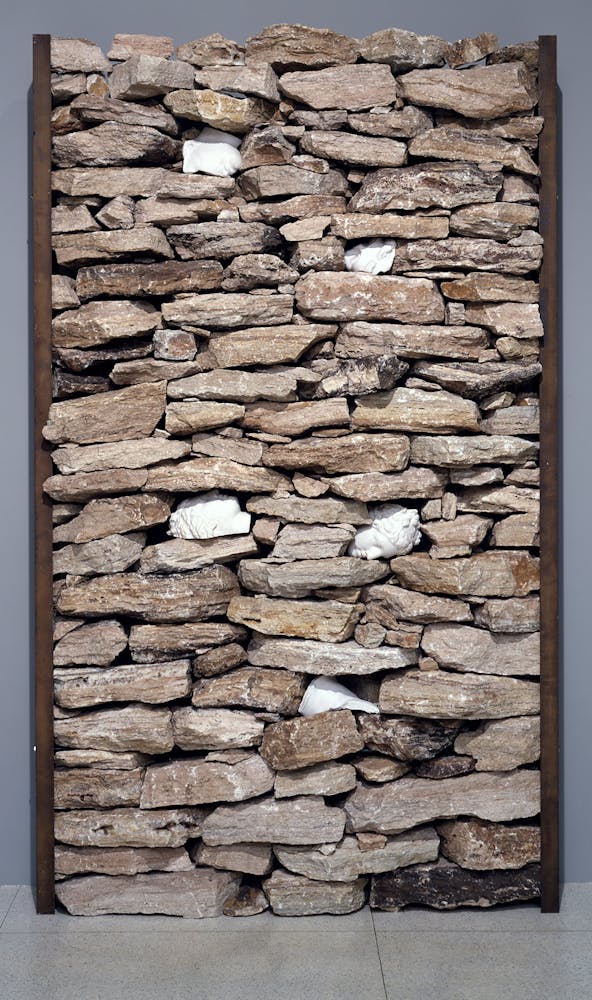 Two boards attached to a gallery wall with stones placed between them approximating a stone wall