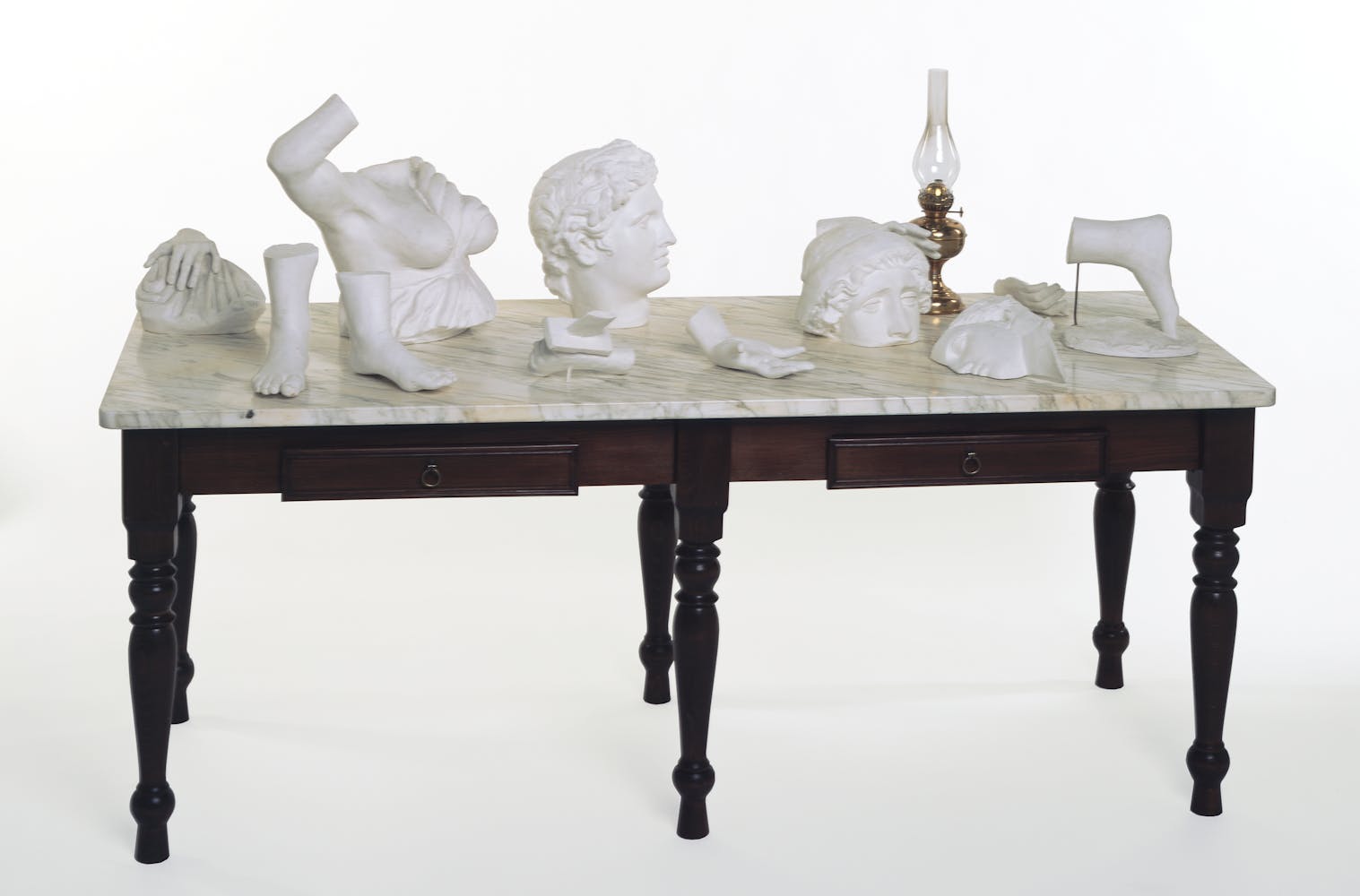 Ornate table with a variety of sculpture objects on top including a white head and lamp