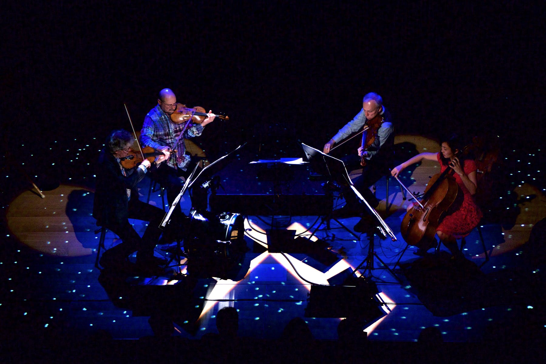 Four musicians on stage facing inwards with star-like lighting